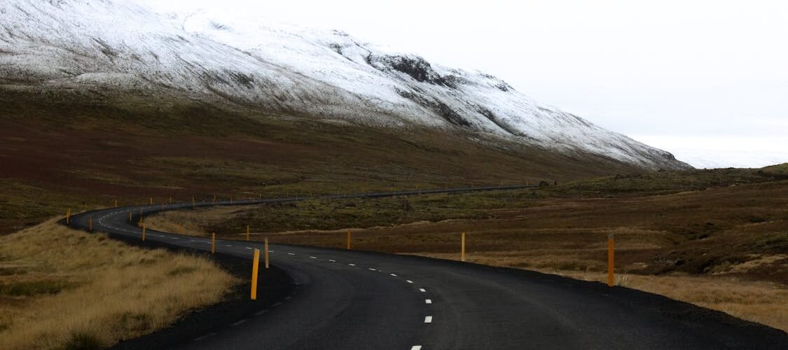 Carretera sinuosa en Islandia con montañas nevadas y paisaje abierto